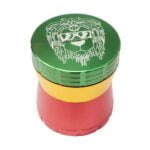 En lille kvadratisk kaffekværn med en diameter på 56 mm præsenteres i et farverigt rasta-design. Overfladen er glat med en kombination af grønne, gule og røde nuancer, der skaber et mønster. Kværnens top har en rund form med en metalknap i midten, og den nederste del har en skridsikker tekstur for bedre greb.