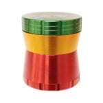 En krydderikværn med en diameter på 56 mm præsentere sig i en farverig rasta-inspireret palette, der inkluderer grøn, gul og rød. Den er fremstillet af metal med en glat overflade, der reflekterer lys. Kværnen har et klassisk design med en skruelås og små perforeringer, der muliggør en jævn kværning af krydderier.