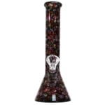 En bongs krop er dekoreret med farverige mexicanske kranier i nuancer af blå, rød og gul. Den har en glat, transparent overflade med en buet form, der afsluttes med en bred, åben top. En smal, lige stilk strækker sig op fra bunden, hvor en lille skål til tobak er placeret. Bunden er stabil og bred.