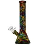 En farverig bong med et pop art-design pryder overfladen. Den er 26 cm høj og fremstår i en kombination af lyse nuancer, herunder rød, blå, gul og grøn. Mønstret består af grafiske elementer og tegneserieagtige billeder. Materialet ser ud til at være glas, med en glat, skinnende overflade og en rund bund, der sikrer stabilitet.