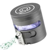 En grå, automatisk krydderigrinder med en slank, cylindrisk form. Overfladen er lavet af rustfrit stål, hvilket giver en glat og skinnende tekstur. Den øverste del har en sort, gummibelagt knap til aktivering. På fronten er der et klart vindue, der afslører indholdet. Bunden er forsynet med en skridsikker gummiring for stabilitet.