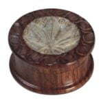 En trægrinder fremstillet af palisander træ præsenterer en dyb brun farve med en glat og skinnende overflade. Den har en rund form med en diameter på 40 mm. Mønsteret i træet viser tydelige årer, der skaber en naturlig struktur. Den har en skruelukning i metal, der er synlig på toppen, hvilket giver et funktionelt element til designet.