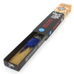 En rustik, træagtig stang af palo santo pryder midten, omgivet af en delikat samling af pinjekerner. Farverne spænder fra mørkebrun til gylden. Overfladen af palo santo har en ujævn tekstur med synlige åretegninger, mens pinjekernerne fremstår glatte og skinnende. Det hele er præsenteret på en lys, neutral baggrund, der fremhæver de naturlige nuancer.