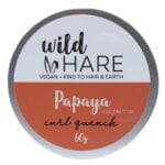 En solid shampoo bar præsenteres i en rund form med en glat, lysebrun overflade, der har en let skinnende finish. Der er små, synlige partikler, der indikerer naturlige ingredienser. På overfladen ses et præg af et logo, der tilføjer et dekorativt element. Størrelsen er kompakt, og den vejer 60 gram.