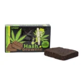 En fudgy brownie med en dyb, chokoladebrun farve og en glat, glinsende overflade. Den er skåret i firkantede stykker, hvilket afslører en let sej tekstur indeni, med små luftbobler synlige. Kanterne er let sprøde, mens toppen er dækket af en let krakeleret skorpe. Kagerne ligger på en neutral, lys overflade, der fremhæver den mørke farve.