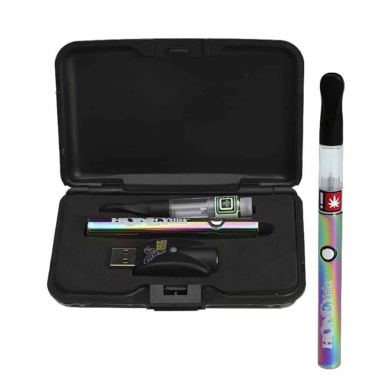 En vape pen præsenterer sig med en slank, cylindrisk form i sølvfarvet metal. Den har en mat overflade og en glat tekstur. Øverst sidder en gennemsigtig beholder, der viser en gylden væske indeni. En rund knap er placeret midt på enheden, omgivet af små ventilationshuller. Nederst ses en USB-port til opladning.