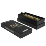 Atmos Tyga Shine Kiln RA Kit i guldudgave præsenterer en elegant, glinsende overflade med en dyb, metallisk gylden farve. Det rektangulære design har skarpe kanter og en glat tekstur, der reflekterer lys. På forsiden findes knapper med klare symboler, der er strategisk placeret for let betjening. Det samlede udtryk er stilrent og moderne.