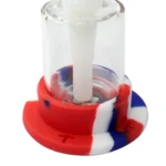 En transparent, farvet bongs struktur i silikone præsenterer en slank, cylindrisk form med en højde på 21 cm. Den har en hexagonal bund, der giver stabilitet. Overfladen er glat med en mat finish, mens indersiden er klar. Der er en tilslutningsport og et glasrør, der stikker ud, hvilket indikerer en kombination af materialer. Farverne varierer fra grøn til blå med nuancer.