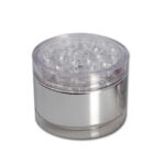 En rund akryl grinder med en diameter på 55 mm. Overfladen er gennemsigtig med en let svag blå nuance. Den har en glat tekstur og en magnetisk lukning. Indvendigt ses skarpe tænder i en stjerneformet konfiguration, der er designet til at male. Grinderens kanter er let afrundede, hvilket giver et strømlinet udseende.