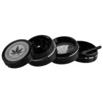 En sort grinder med en blank overflade og en diameter på 40 mm. Grinderens top har en let buet form, og en skridsikker tekstur pryder kanten. Indvendigt ses skarpe tænder, der er designet til at male urter. Der er en subtil reflektion af lys på den glatte overflade, hvilket fremhæver dens enkle, elegante design.