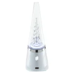 En koncentrat vaporizer præsenterer sig med en glat, gennemsigtig krystalformet beholder i klar plast, der er prydet med en metallisk sølvfarvet base. En lys, blød belysning fremhæver en indvendig perle, der ses i en dyb blå nuance. Enhedens knapper er placeret diskret på siden, og der er et lille logo indgraveret på basen.