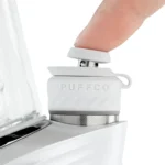 Puffco Peak Pro Pearl er en elegant vaporizer i et slankt design. Den har en glat, sort overflade med en mat finish, der fremhæver dens moderne linjer. En transparent skål i midten er synlig, der lader lys skinne igennem. Knappen er diskret placeret, og et lysende LED-indikatorpanel viser forskellige funktioner. En stilfuld, minimalistisk æstetik pryder enheden.