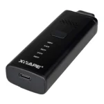 En kompakt vaporizer med en slank, rektangulær form. Huset er dækket af et mat sort materiale, der giver en moderne og stilren finish. Foran findes en digital skærm med tydelig tekst og et par knapper til justering. En røgkanal strækker sig fra toppen, og en silikonebelægning pryder den øverste del, hvilket sikrer et godt greb.
