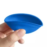 En lille blandeskål i silikone præsenteres i en blanding af blå og pink farver. Skålen har en glat, fleksibel overflade med en rund form og en diameter på 7 cm. Den har en let bredere kant, der giver mulighed for nem håndtering. Indersiden er ensfarvet blå, mens ydersiden prydes af et pink mønster. Texturen er blød og bøjeligt, hvilket karakteriserer silikonematerialet.