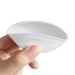 En lille skål i silikone med en rund form, der måler 7 cm i diameter. Skålen har en blød, glat overflade i hvid farve, mens kanten og indersiden er accentueret med en lys grøn farve. Den er fleksibel og bøjeligt, hvilket gør den nem at håndtere. Bunden er flad og stabil, hvilket giver en sikker placering.