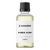 En transparent flaske med en mørkebrun væske, der indeholder terpenes, præsenteres. Flaskens hals er smal og afsluttes med en sort, skruelukning. Etiket på flasken er hvid med grøn og sort tekst, der angiver produktets navn og indhold. Flasken står på en lys overflade, hvilket skaber kontrast til den mørke væske.