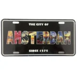 Et rektangulært metalskilt præsenterer teksten "Amsterdam" i store, hvide bogstaver med en sort kontur. Baggrunden er i en dyb blå nuance, der giver kontrast til teksten. Skiltets kanter er let afrundede, og overfladen har en glat, skinnende finish, der reflekterer lys. Ingen yderligere dekorative elementer eller mønstre er til stede.