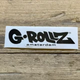 G-Rollz-logoet præsenterer sig med en strømlinet, moderne skrifttype i sort, der udstråler enkelhed. Bogstaverne er tydelige og sans-serif, hvilket giver et minimalistisk udtryk. Logoet er placeret på en ensfarvet baggrund, der fremhæver kontrasten mellem det sorte logo og den lysere overflade. Ingen yderligere grafiske elementer eller dekorationer komplikerer designet.
