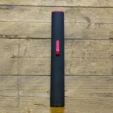 En lang, flad lighter præsenteres med en glat, metalisk overflade i en dyb sort farve. Den har en rektangulær form med afrundede kanter. Toppen indeholder en gnistmekanisme og en låg, der åbnes for at afsløre en refill-port. På siden er der små, indgraverede symboler og en skridsikker tekstur, der sikrer et godt greb.