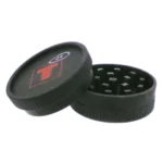 En kompakt grinder med en diameter på 53 mm, fremstillet af aluminium med en børstet metaloverflade. Den har en klassisk cylindrisk form med skarpe tænder indvendigt, der er designet til at male. Låget har en magnetisk lukning i midten, og der er ingen synlige knapper eller symboler. Den er praktisk og funktionel i sit design.