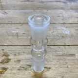 Scott bonghovedadapteren har en klar, transparent krop med glatte, afrundede kanter og et isfangsystem, der har en ribbet tekstur. Den er fremstillet af glas, hvilket giver en glansfuld overflade. Adapterens tilslutningspunkter er præcise, og der er synlige, fine detaljer omkring åbningerne, der sikrer en tætsiddende pasform.