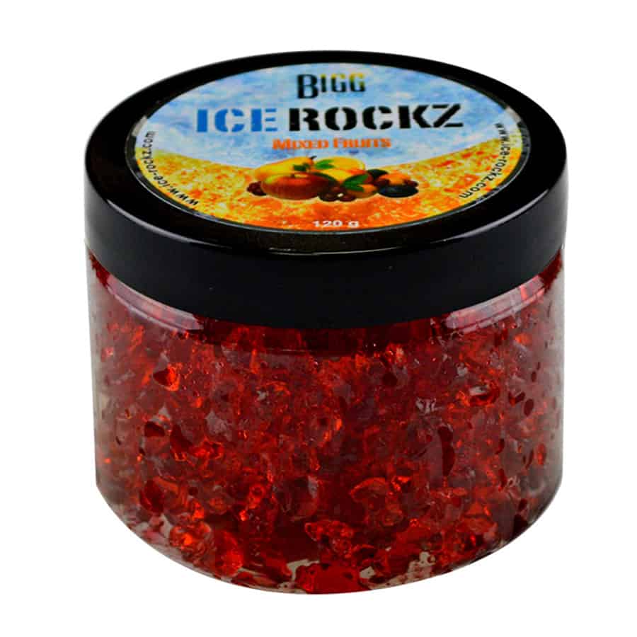 En transparent emballage indeholder en blanding af små, farverige frugtsmage i form af isterninger. Farverne inkluderer orange, rød, gul og grøn, hvilket skaber et livligt udtryk. Isterningerne har en glat overflade med lette skygger, der fremhæver deres former. Øverst på emballagen er der en tydelig logo-tekst, der præsenterer produktnavnet.