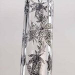 En sort, glat beaker med en høj, cylindrisk form pryder midten. Beakeren er dekoreret med et stjerneformet mønster, der gløder i en lysende nuance. Overfladen har en blank finish, hvilket skaber en flot refleksion. Beakeren står stabilt på en bred, flad bund, der tilføjer stabilitet til designet.