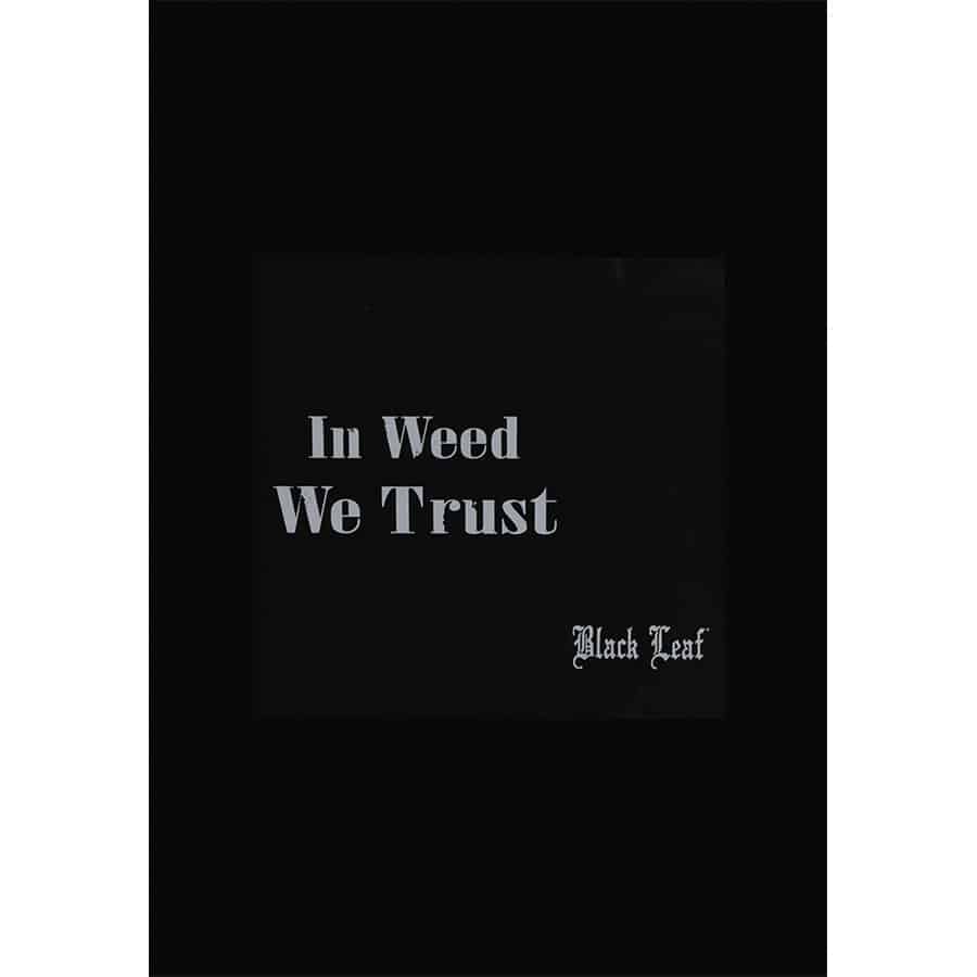 Et rektangulært blandingsbakke med en mørk overflade prydet af et stiliseret bladmotiv i guld. Bakken har afrundede kanter og en blød, glat tekstur. Motivet indeholder teksten "In Weed We Trust" i en elegant skrifttype, der også er i guld. Baggrunden er ensartet og fremhæver detaljerne i designet.