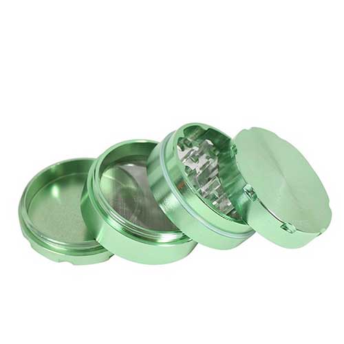 En grøn, cylindrisk krydderikværn med fire lag. Overfladen har en glat, mat tekstur, mens de indre lag præsenterer et ribbet mønster for effektiv kværning. Øverste del har en skruefunktion med en rund, let fremhævet knap. Kværnen har små lufthuller for at sikre cirkulation. Farven er ensartet og jævn, uden synlige mærker.