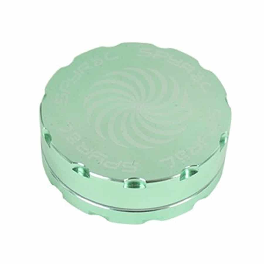 En grøn, to-delt krydderikværn med en diameter på 62 mm. Kværnen har en glat, mat overflade og en rund form. Den øverste del har et let skrånende design med en central, firkantet åbning. Der er små, runde huller i bunden af den nederste del, der muliggør udslip af kværnede krydderier. Farven er ensartet og livlig.