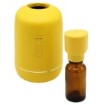 En moderne nebulizer præsenterer sig i en slank, cylindrisk form med en mat hvid overflade. Den har en rund bund og en let skrånende top, hvor en lille åbning til dampudledning er synlig. En diskret knap i sølvfarvet metal sidder på siden. Designet er minimalistisk, uden synlige ledninger, hvilket giver et stilrent udtryk.