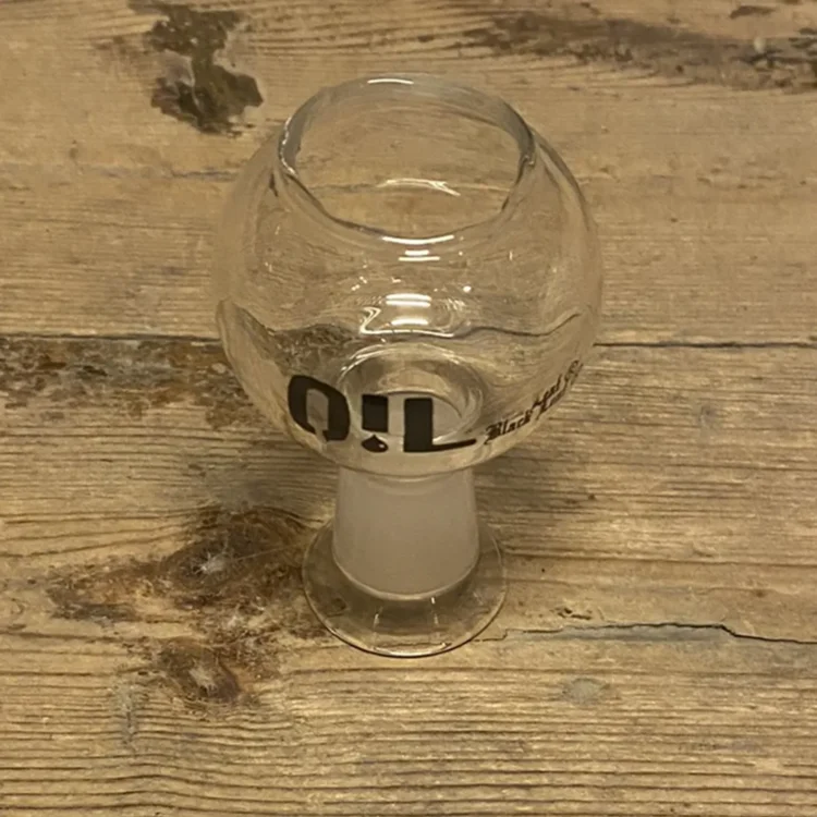 En sort dab bowl fremstår med en glat, blank overflade og en rund form. Den har en dyb skål med en let skrånende kant, der skaber en elegant silhuet. Materialet ser ud til at være glas, med fine detaljer i form af et bladmotiv, der tilføjer et subtilt præg. Farven er ensartet sort, hvilket giver et moderne udtryk.