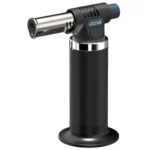 En butanblæser præsenteres med en slank, cylindrisk form og en sort mat overflade, der giver et moderne udseende. Det har en ergonomisk håndtag med en tekstur, der sikrer et godt greb. Foran er der en gennemsigtig brændstoftank, der viser indholdsniveauet. En justerbar dyse og en tændingsknap er placeret på siden, hvilket giver præcise justeringer af flammen.