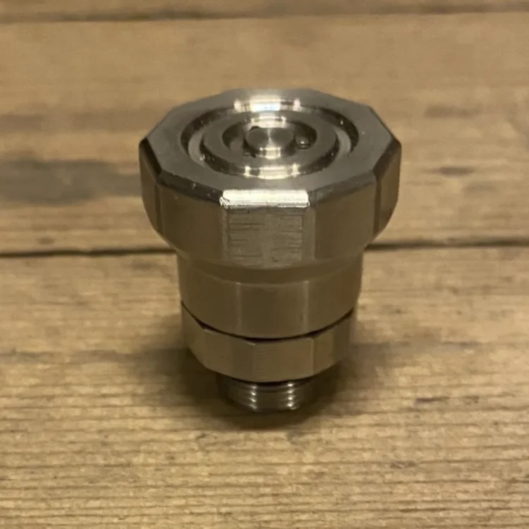 Vandpibeventilen er udført i metal med en glansfuld overflade, der reflekterer lys. Den har en kugleformet mekanisme i midten, som er omkranset af en cylinder. Ventilen er forsynet med en skruegevind i bunden for fastgørelse. Farven er primært sølvgrå med indslag af sort ved gevindet. Det samlede design fremstår enkelt og funktionelt.