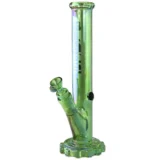 En bongs cylindriske krop er fremstillet af klart glas med en grøn, glinsende geardesign på siden. Den har en bred, stabil bund og en smal hals, der afsluttes med en rund åbning. En perkolator er placeret i midten, hvilket skaber en kompleks struktur. Den grønne farve tilføjer et dekorativt element til det gennemsigtige glas.