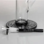 En 48 cm høj bong i klart glas, prydet med en dybgrøn dekorativ kant. Den har en kompleks konstruktion med en tiarmet perkolator, der skaber en blød rygeoplevelse. Bongen har en rund fod og en bred hals, som afsluttes med en buet mundstykke. Overfladen er glat, og der er synlige vandkamre, der giver en visuel dybde.