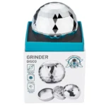 En metalgrinder med en diameter på 65 mm, prydet med en skinnende overflade i sølvfarve. Grinderens krop har en glat, poleret tekstur, mens toppen har et indgraveret mønster med små huller til knusning. Knivene indeni er skarpe og vinklede, hvilket sikrer effektiv malning. Den har en skridsikker kant for bedre greb og en lille magnetisk lukning.