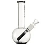 En rund tube med en højde på 18 cm præsenterer sig i klart glas. Den har en cylindrisk form med en bredere bund og en smalere top, der afsluttes med en fordybning til et mundstykke. Basisfarven er gennemsigtig, med subtile grønne nuancer langs kanten. En enkelt vandbeholder er synlig, og der er en lille, integreret skål til indholdet.