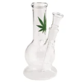 En gennemsigtig bong med en cylindrisk form, der måler 15 cm i højden. Den har en let buet hals og en bred bund, hvilket giver stabilitet. Materialet er klart glas med en glat overflade, der reflekterer lys. En indbygget skål til tobaksprodukter sidder på siden, og der er en lille, rund åbning i toppen til indånding.