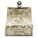 En solid shampoo bar præsenteres i en oval form med en glat, blød overflade. Farven er en varm, gylden beige nuance, der giver en naturlig fornemmelse. Overfladen har en let glans, mens der er indgraveret tekst, som angiver produktets navn. Den kompakte størrelse gør den let at håndtere, og den fremstår som en miljøvenlig alternativ til flydende shampoo.