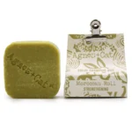 En solid shampoo bar i en rund form præsenterer sig med en glat, beige overflade og en let struktureret tekstur. Den har en naturlig finish og fremstår uden synlige urenheder. Overfladen er ensartet, og der er en minimal skrift med information om produktet præget ind i baren, hvilket tilføjer et subtilt design.