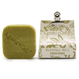 En solid shampoo bar i en rund form præsenterer sig med en glat, beige overflade og en let struktureret tekstur. Den har en naturlig finish og fremstår uden synlige urenheder. Overfladen er ensartet, og der er en minimal skrift med information om produktet præget ind i baren, hvilket tilføjer et subtilt design.