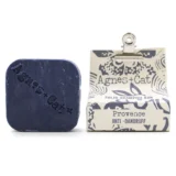 En solid shampoo bar præsenteres med en rund, flad form. Overfladen er glat og ensartet, i en lys, cremet farve. Mørkere nuancer skaber subtile skygger, hvilket giver en let tekstur. En enkelt, let præget tekst på overfladen tilføjer detaljer. Shampoo baren ligger på en naturlig, ubehandlet træoverflade, der komplementerer det minimalistiske udtryk.