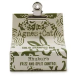 En solid shampoo bar med en rund, flad form og en dyb rødlig farve, der minder om rabarber. Overfladen er glat, men har subtile teksturer og et let skinnende finish. Ingen synlige emballageelementer eller påskrifter er til stede, hvilket fremhæver det minimalistiske design. Shampoo baren er placeret på en naturlig, ubehandlet træflade.