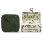 En solid shampoo bar præsenterer sig i en oval form med en glat overflade. Farven er en dyb, varm rabarbernuance, der strækker sig fra lysere til mørkere toner. Strukturen er kompakt og ensartet uden synlige urenheder. Der er en let glans, som indikerer en fugtig tekstur, og baren har ingen synlige emballager eller etiketter.