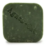 En solid shampoo bar præsenteres i en rektangulær form med afrundede kanter. Overfladen har en glat tekstur og en varm, rødbrun farve med lette, lyse striber. Der er indgraveret tekst på den ene side, der angiver produktets navn. Baren ligger på en neutral, lys overflade, der fremhæver dens farve og form.