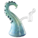 En olie-bong med en højde på 17 cm præsenterer sig i klar glas med en dyb blå farve og et bølgende tentakelmønster. Den har en glat overflade og en bred fod, der giver stabilitet. En skål til urter sidder på siden, mens en smal hals strækker sig opad. Farverne skaber en klar kontrast mod det gennemsigtige materiale.