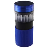 En sort grinder er centralt placeret, med en glat overflade og en lille diameter. Den har en let buet form og er dekoreret med et bladmønster. Ved siden af ligger en cone-filler, der har en blå farve og en cylinderform. Begge elementer er lavet af metal, hvilket giver en skinnende finish, der reflekterer lys.