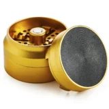 Grinderen præsenterer en gylden overflade med en glat, blank finish, der reflekterer lys. Den har en cirkulær form med en diameter på 55-63 mm. Mønstret på toppen er detaljeret med indgraverede linjer, der skaber en struktureret tekstur. Indvendigt findes skarpe tænder i metal, designet til effektiv nedmaling. Kanten er let skrånet for bedre greb.