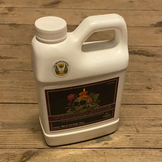 En transparent plastflaske med en sort skruelåg. Flasken rummer en mørk, nærmest ravfarvet væske. Etiketens design præsenterer farverne grøn, hvid og sort med grafiske elementer og tekst i forskellige skrifttyper. Nederst på etiketten er der en dato, der angiver udløbsdatoen. Flaskens form er cylindrisk med en let buet hals.